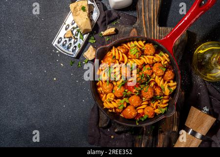Fusilli pasta with meatballs in tomato vegetable sauce, on dark background with herbs and grated cheese, top view copy space Stock Photo