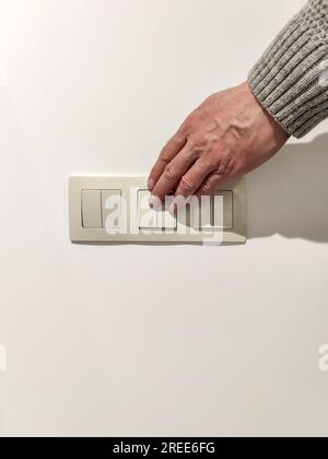 Man turns on the light. Man's hand in gray sweater presses light switch. Close-up. selective focus. Stock Photo