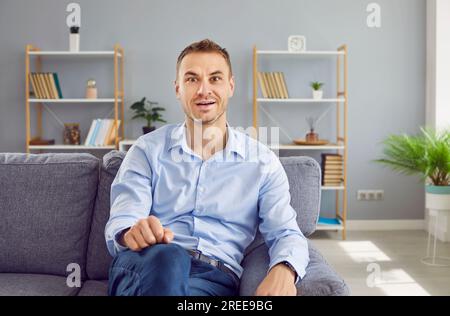 Man sitting on a sofa and looking at the camera with a funny, surprised, happy face expression Stock Photo