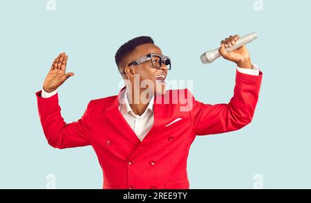 Extravagant man in suit singing song in microphone while performing on pastel light blue background. Stock Photo