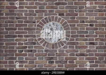 multi-colored brick wall with a brown and white marble circular medallion in the center, flemish bond bricklay pattern in earth tones, beige, brown Stock Photo