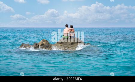Young couple sitting on a cliff in the middle of the sea Stock Photo