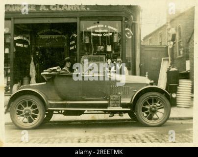 Original 1920's era small postcard Maurice A. Clarke Ironmongers / hardware shop -small family run business -  proprietor's wife sits in car, Morris Cowley 'Bullnose' open 2 seater - possibly showing off the new family car. London U.K. Circa 1925. Stock Photo