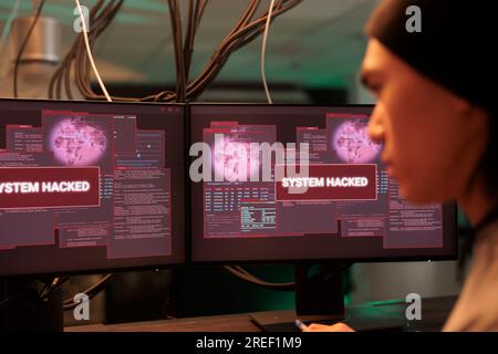 Asian thief analyzing encryption alert on monitors, working to break into government system late at night. Young person planting malware to crack security code, stealing passwords. Stock Photo