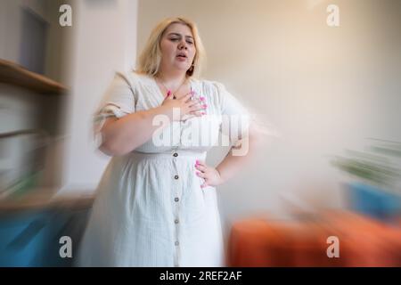 Overweight plus size young woman feel chest pain at home. Heart attack concept. Stock Photo