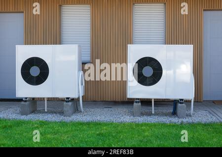Two high-efficiency air source heat pumps installed on the exterior of a contemporary home, utilizing green electricity for sustainable heating soluti Stock Photo