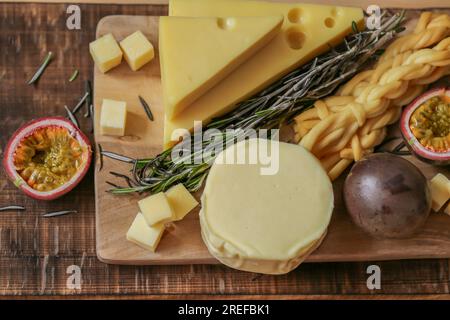 Cheese assorted cut on a wooden board with herbs and fruits.Hard and soft cheeses, rosemary and passion fruit. Mazdar cheese triangles, gouda cheese Stock Photo