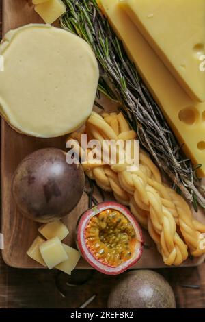 Mazdar cheese triangles, gouda cheese cubes,chechil smoked.Cheese assorted cut on a board with herbs and fruits.Hard and soft cheeses, rosemary and Stock Photo