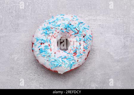 Sweet glazed donut decorated with sprinkles on light grey table, top view. Tasty confectionery Stock Photo