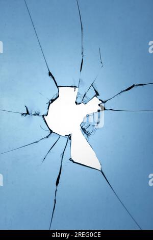Glass texture of a broken window with a hole and cracks on a blue background Stock Photo