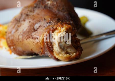 Roasted pork knuckle, pork knee served with pickled cucumbers and herbs, cabbage and mustard Stock Photo
