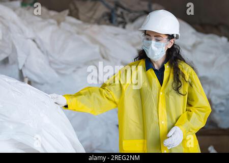 Black-haired lady worker in mask sorts trash at waste plant Stock Photo