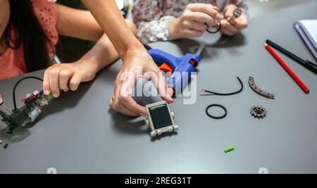 Female hand showing solar panel while students assembling machine pieces Stock Photo