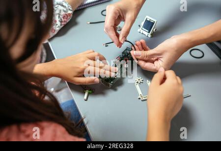 Female teacher helping girl student to assemble electrical circuit in a robotics class Stock Photo