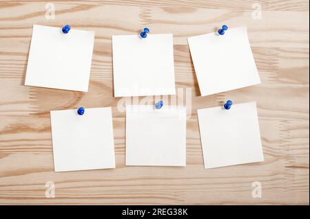 Six white paper notes mockup pinned to wooden bulletin board. sticky notes on bulletin board. Three sticker with push pins on wooden background Stock Photo