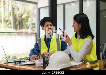 Two young man and woman engineers meeting, working, discussing, planing, designing, measuring layout of building blueprints in construction site floor Stock Photo