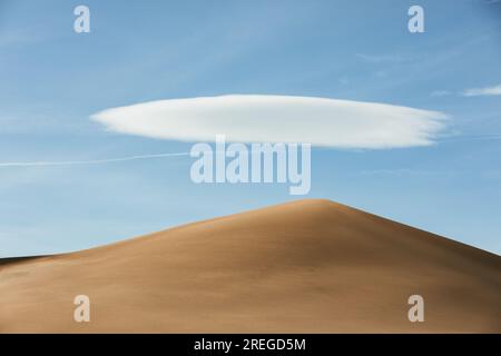golden tan sand dune under blue sky with one puffy white cloud Stock Photo