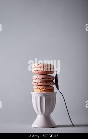 Macarons stacked in a egg cup, fork on the side on gray background Stock Photo