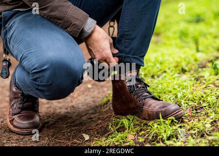 Detail of man adjusting pant leg with focus on leather hiking boots Stock Photo