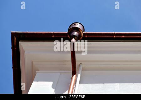 shiny new copper gutter rain water leader, downspout detail. home renovation and construction closeup. textured stucco exterior. roof edge. blue sky. Stock Photo