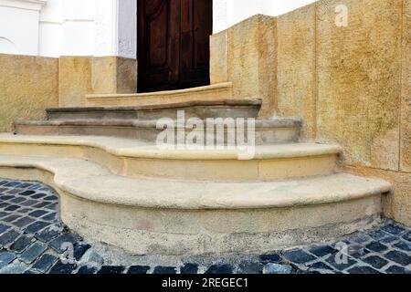 curving old stone stairs. closeup view. bright lights and shadows. background image. cobble stone pavement. brown wood door. diminishing perspective Stock Photo