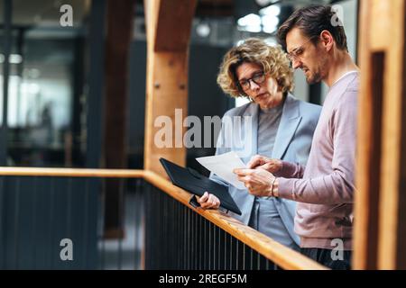 Two business colleagues discussing a document in an office. Professionals analysing a report. business man and business woman stand together on an int Stock Photo