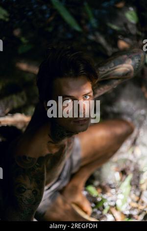 Young tattooed man in tropical jungle, rays of light. Stock Photo