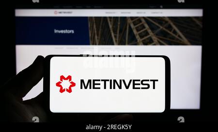 Person holding smartphone with logo of steel company Ukrainian Metinvest Holding LLC on screen in front of website. Focus on phone display. Stock Photo