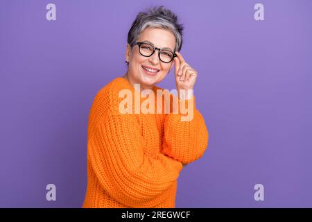 Portrait of satisfied business old lady wearing orange knitted sweater touch her classic glasses boss isolated on violet color background Stock Photo