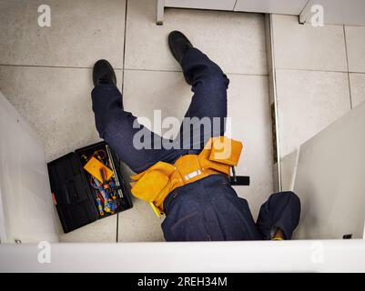 Kitchen, maintenance and repair with a plumber on the floor of a home to fix a leak, issue or problem. Plumbing, renovation and tools with a handyman Stock Photo