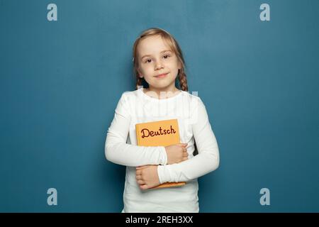 Child student girl with German language book on the background of blue chalkboard Stock Photo