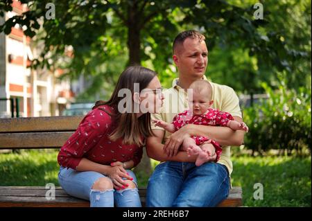 Family with little baby girl sitting on a bench in a park Stock Photo