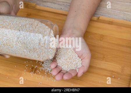 Hand holding glass jar containing puffed amaranth or ramdana or rajgira on a wooden tray. It is a gluten free grain that provides fiber Stock Photo