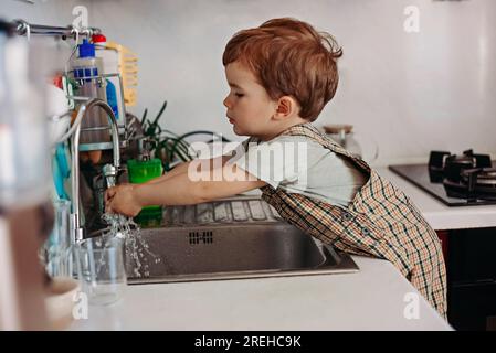 The boy washes his hands in the kitchen. Stock Photo