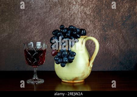 Old earthenware wine jug with glass of wine and grapes on a polished wooden surface Stock Photo