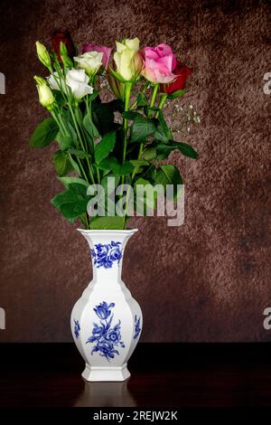 Assorted fresh flowers in a white and blue ceramic flower vase on a wooden surface Stock Photo