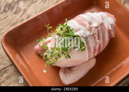 A raw, uncooked chicken fillet on the bone quarter that has been wrapped in streaky bacon and flavoured with fresh thyme. It will be simmered in white Stock Photo
