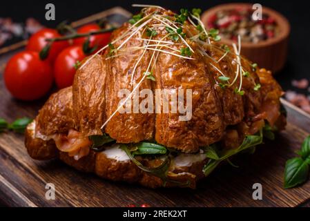 Delicious crispy croissant with salmon, lettuce, cheese and tomatoes on a dark concrete background Stock Photo