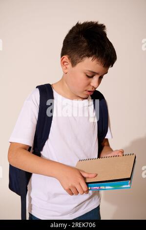 Vertical studio portrait of a Caucasian serious teenage schoolboy in white mockup t-shirt and blue jeans, holding copybooks, isolated over white backg Stock Photo