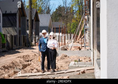Woman general designer and foreman in hardhats standing near builded house Stock Photo