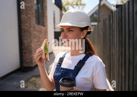 Woman building engineer eating sandwich and drinking coffee to-go Stock Photo