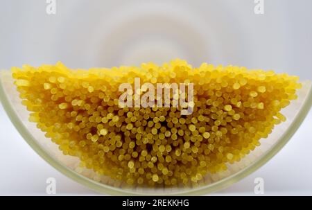 A view of some spaghetti in a tall glass container laying on it's side without the lid on photographed against a white background. Stock Photo