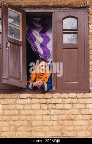 Khansahib Tehsil, Jammu and Kashmir, India. October 31, 2022. Smiling woman in the window of a house. Stock Photo