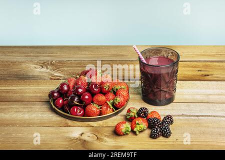 Detox fruit still life of ripe red berries, small strawberries, black mulberries, cherry cherries with juice in a cut crystal glass on unvarnished woo Stock Photo