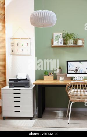 Stylish workplace with computer, printer and houseplant near olive wall at home Stock Photo
