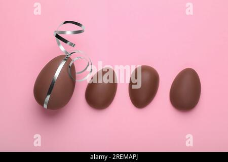 Whole and halves of chocolate eggs on pink background, flat lay Stock Photo
