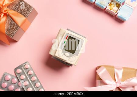 Blood pressure monitor, pills and boxes on pink background, flat lay. Medical gift Stock Photo