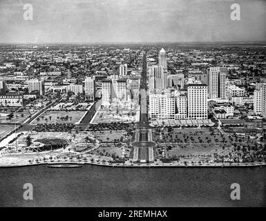 Miami, Florida  c. 1930 Looking up Flagler Street at downtown Miami with Miami Park and the waterfront in the foreground. The McAllister Hotel is on the right side of Flagler Street in the forefront. Stock Photo