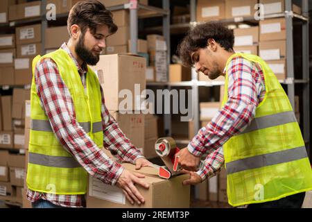 Male warehouse workers sealing cardboard boxes in distribution centre. Stock Photo