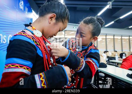 (230729) -- CHENGDU, July 29, 2023 (Xinhua) -- Jihelazuo (R) helps Edirehan with her costume prior to rehearsal of the opening ceremony in Chengdu of southwest China's Sichuan Province, on July 23, 2023. Six children dressed in traditional Yi ethnic costumes choired a song to inaugurate the opening ceremony of the 31st summer edition of the FISU World University Games. Jihaoyouguo, Jihelazuo, Ma Jieying, Edirehan, Jiziyisheng and Jiduoshila came from Zhaojue County, Liangshan Yi Autonomous Prefecture, southwest China's Sichuan Province. Despite their age differences, they all share a common ho Stock Photo